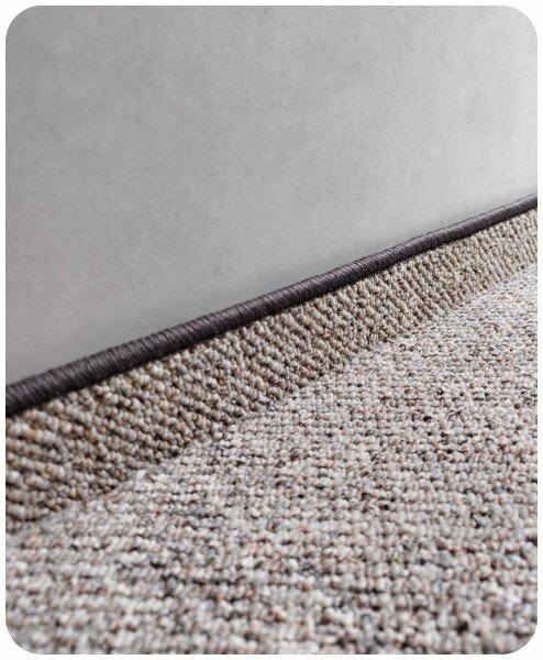 Braune Teppichleiste mit umnähten Rand an einer grauen Wand