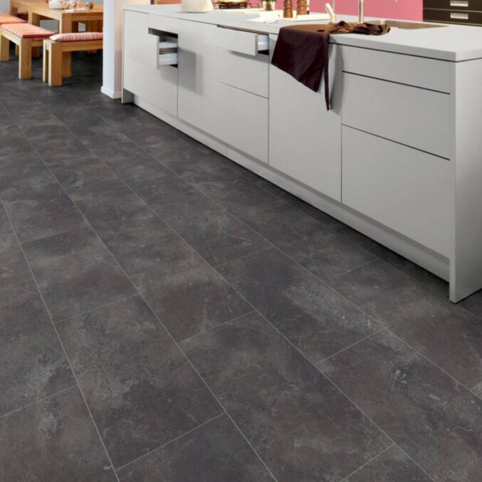 Raumfoto eines Laminats in einer Küche. Das Laminat hat eine schwarze Fliesenoptik mit grauen Elementen. Die Dielen sind besonders breit.
