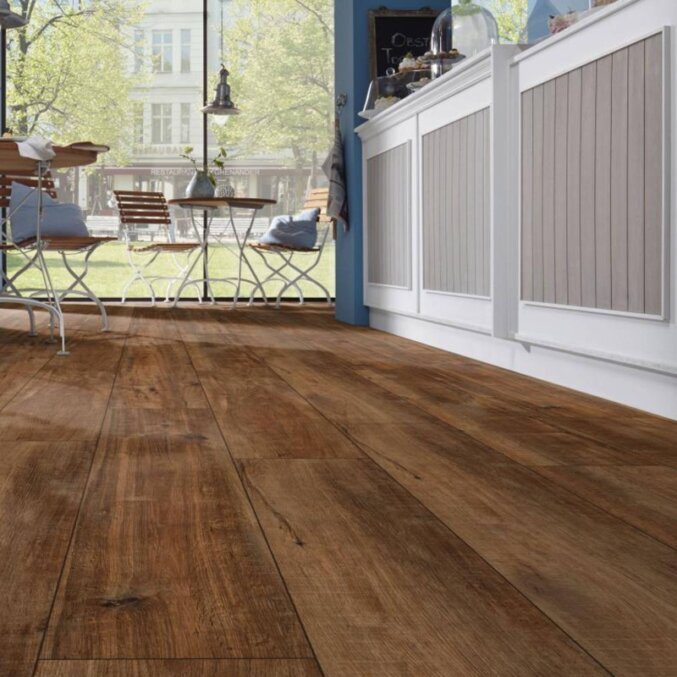 Raumfoto eines Laminats mit breiten Dielen in dunkelbrauner Eichenholzoptik in einer Küche mit dunklen Furchen.