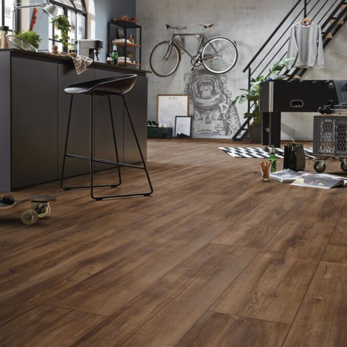 Raumfoto eines Laminats in einem Mehrzweckraum. Das Laminat hat eine eher rustikale Eichenholzoptik und breite Dielen. Gefärbt in einem sehr dunkelbraunen Farbton.