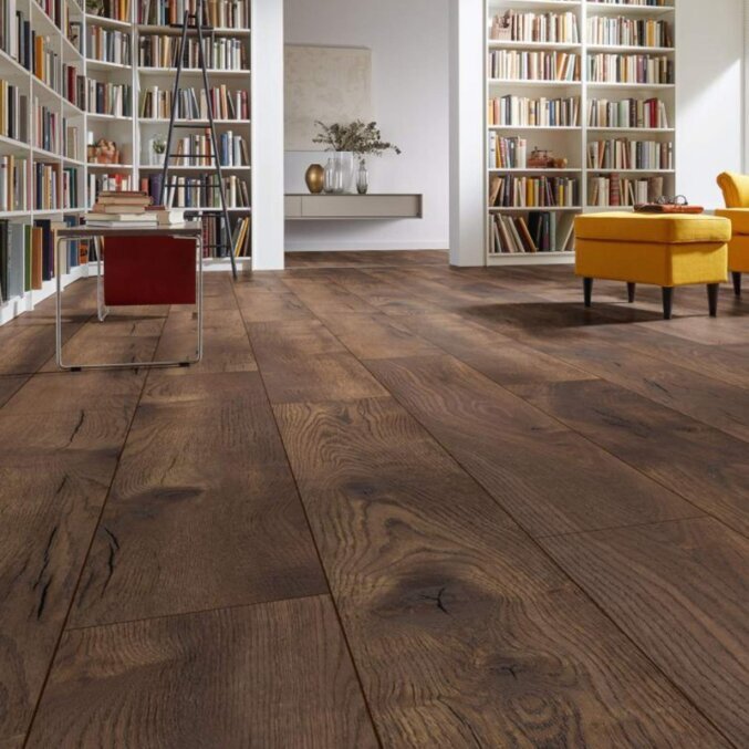 Raumfoto eines Laminats in einem Raum voller Bücher. Das Laminat hat eine rustikale Eichenholzoptik mit klaren Furchen und Rissen und breite Dielen. Gefärbt in einem sehr dunkelbraunen Farbton.