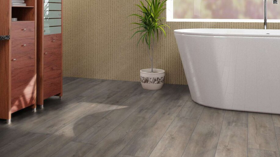 Laminat in grauer Holzoptik in einem Badezimmer. Im Hintergrund sind dunkelbraune Schränke sowie eine moderne weiße Keramikbadewanne.